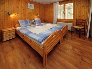 Ein Schlafzimmer mit Holzvertäfelung, einem Bett, einem Nachttisch, einem Sessel und einem Fenster mit Vorhängen.