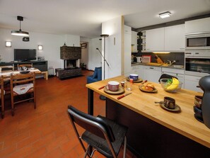 Une cuisine moderne avec une cheminée en pierre, un coin repas avec des chaises en bois et un téléviseur.