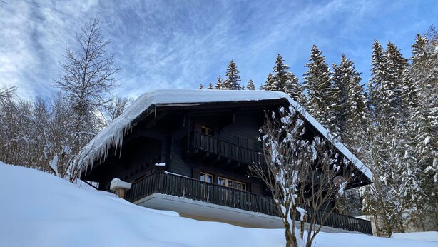 Een chalet met balkon, omringd door besneeuwde bomen en een heldere lucht.