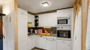 Een compacte keuken met witte kastjes, een magnetron, een oven en een spoelbak.