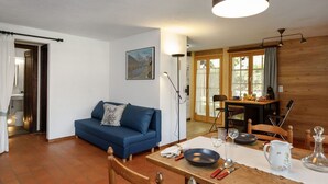 Een gezellige woonkamer met een blauwe bank, een eettafel gedekt met borden, glazen en bestek, en een keuken zichtbaar door een open deur.