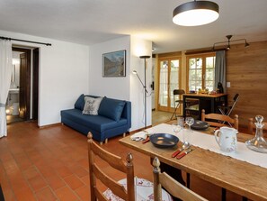 Ein gemütlicher Wohnbereich mit einem blauen Sofa, einem Esstisch mit Tellern, Gläsern und Besteck, und einer durch eine offene Tür einsehbarer Küche.