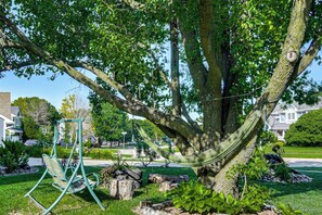 A hammock tied to a large tree in a well-maintained garden with a swing set and a house in the background. - Endless Fun! Family Home w/ Spacious Yard in Clive (Clive)