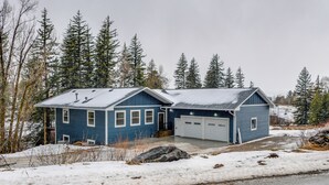 A two-story blue house with a garage, surrounded by snow-covered ground and trees. - Mountain Retreat By the River: Star Valley Getaway (Afton)