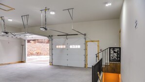 A spacious garage with a large white door, a wooden staircase, and a metal ceiling structure. - Mountain Retreat By the River: Star Valley Getaway (Afton)