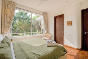 A bedroom with a large window, a bed with green bedding, a chair, and a door. - Vida Pacifica Villa (Verla Canca)