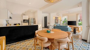 Une cuisine moderne avec un plan de travail noir, un coin repas avec une table ronde et des chaises, et un salon équipé d’un téléviseur et de sièges confortables.