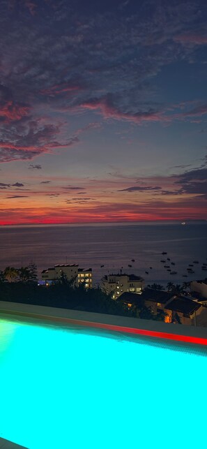 Une vue sur la côte, avec un coucher de soleil, une piscine et des bâtiments au premier plan.