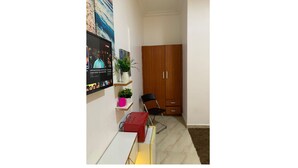 A room with a wooden wardrobe, a desk with a red box, a black chair, and a shelf with plants. - Cozy 1-bedroom house with 247 power, FREE Wifi, Netflix, AC (Lekki)