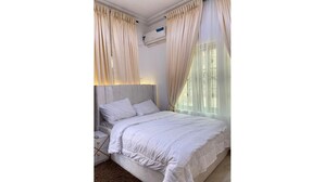 A bedroom with a bed, nightstand, and an air conditioning unit. - Cozy 1-bedroom house with 247 power, FREE Wifi, Netflix, AC (Lekki)
