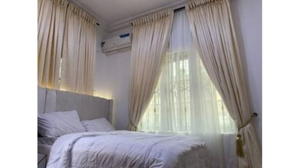 A bedroom with a bed, curtains, and an air conditioning unit. - Cozy 1-bedroom house with 247 power, FREE Wifi, Netflix, AC (Lekki)