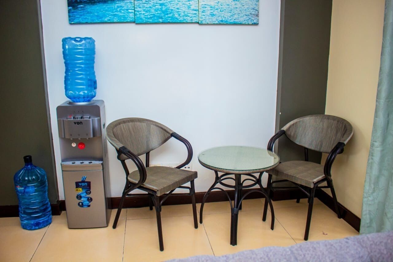 A small room with a water dispenser, two wicker chairs, a round table, and a large water bottle.