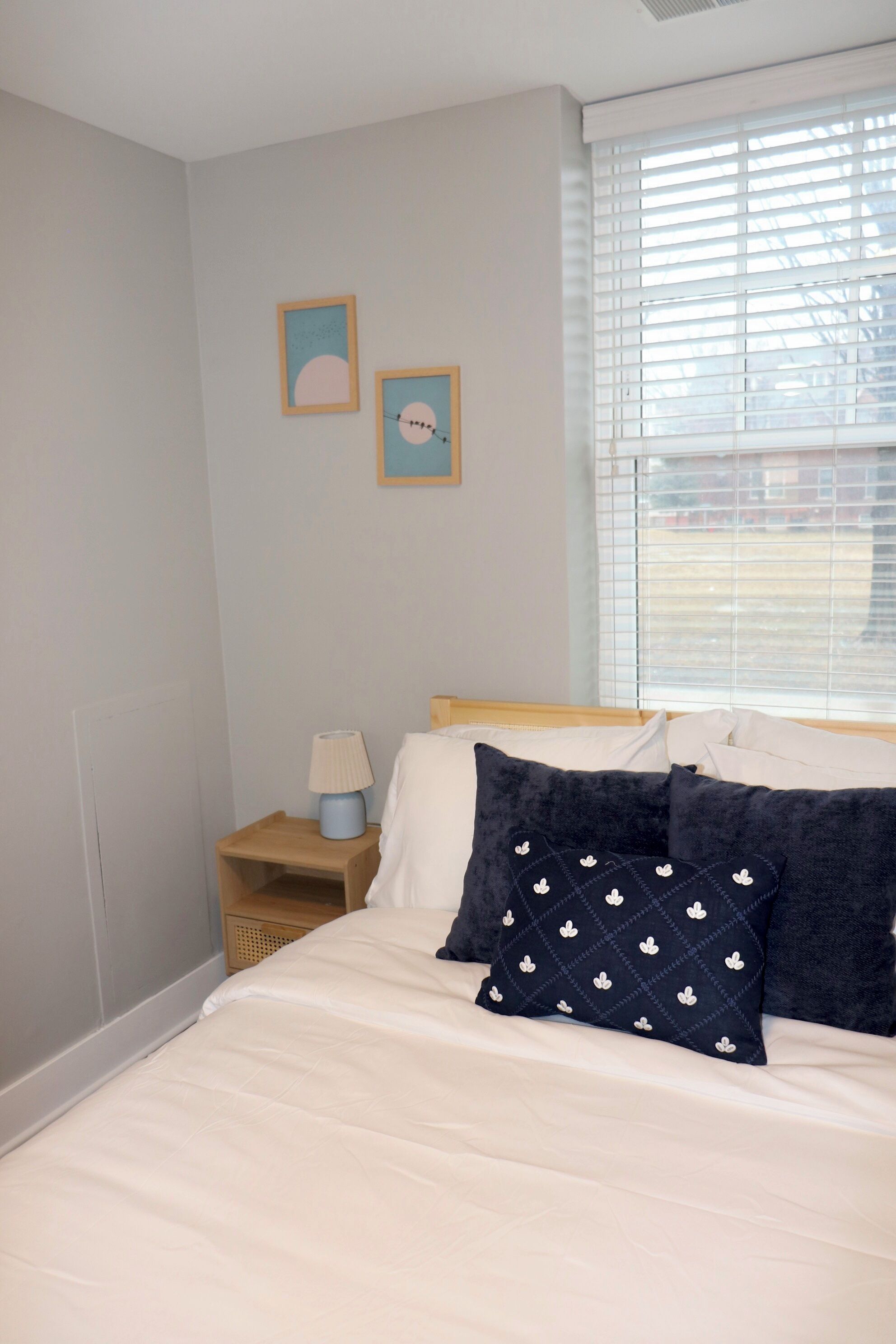 Une chambre à coucher avec un lit, une table de chevet, une lampe et deux tableaux encadrés accrochés au mur.