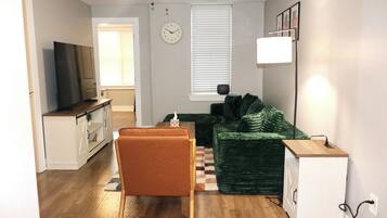 A living room with a sofa, a small table, a television, and a clock on the wall.