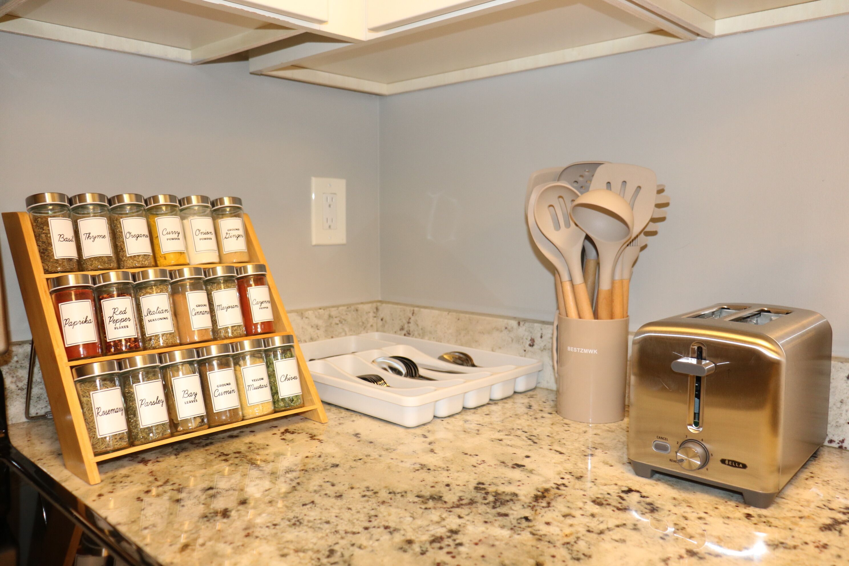 Una cocina con un especiero, un tostador y un juego de utensilios de madera.
