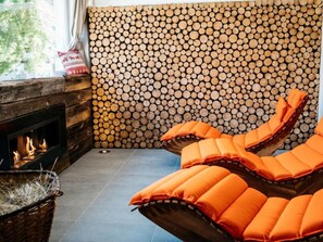 Een gezellige hoek met een open haard, een houten wand en twee fauteuils met oranje kussens.