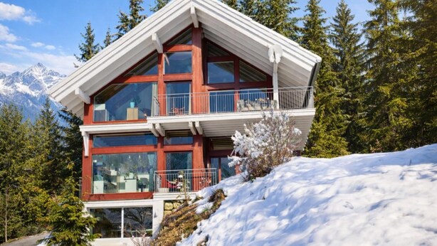 A modern multi-story building with large windows, a balcony, and a view of snow-covered mountains.