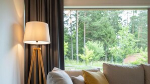 A room with a sofa, a floor lamp, and a view of trees through a window.