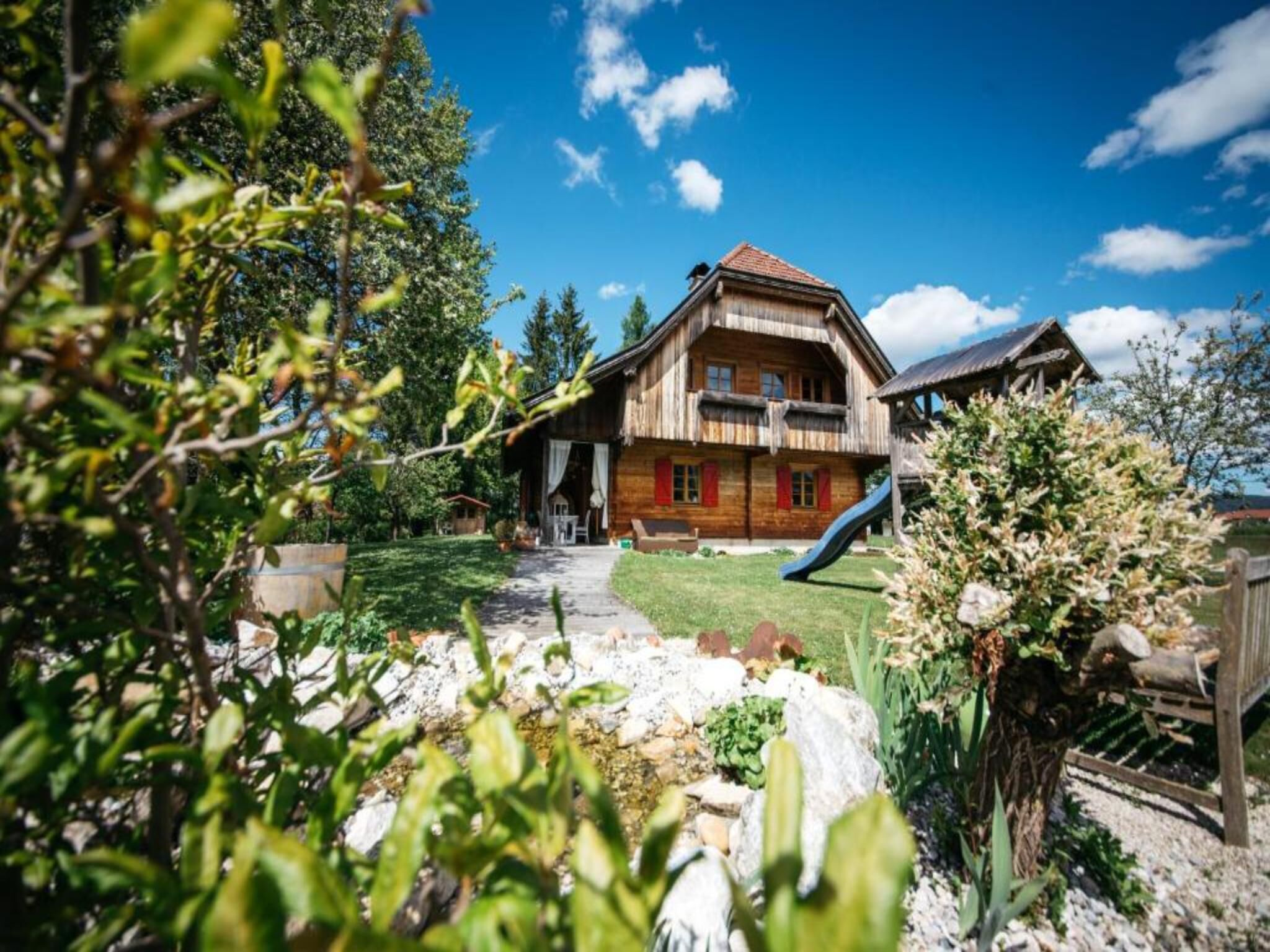 Eine Holzhütte mit einem großen Balkon, einer Rutsche und einem gepflegten Garten.