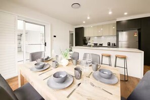 A modern kitchen with dark cabinets, a stainless steel refrigerator, and a dining area with a wooden table set for four. - Brand new 3BR townhouse -Modern comfy family home (Rochedale)