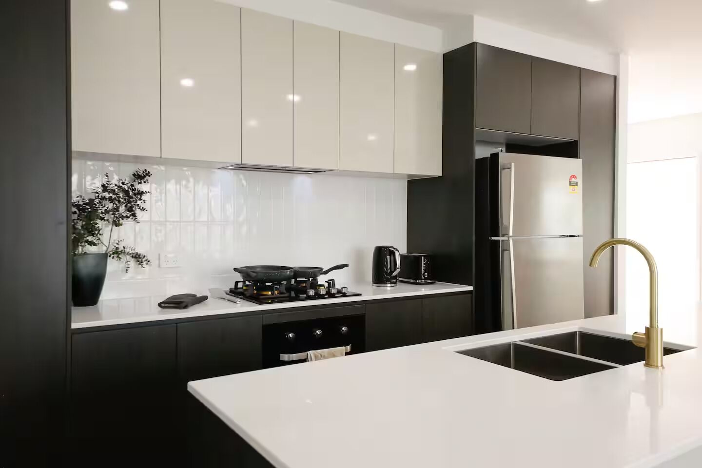 A modern kitchen with a white countertop, black cabinets, a stainless steel refrigerator, and a gold faucet.