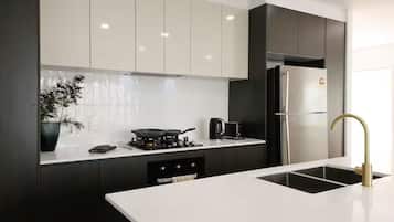 A modern kitchen with a white countertop, black cabinets, a stainless steel refrigerator, and a gold faucet.