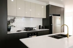 A modern kitchen with a white countertop, black cabinets, a stainless steel refrigerator, and a gold faucet. - Brand new 3BR townhouse -Modern comfy family home (Rochedale)