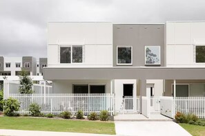 A modern two-story residential building with a white exterior, large windows, and a white fence surrounding the property. - Brand new 3BR townhouse -Modern comfy family home (Rochedale)