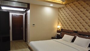 A hotel room with a large bed, a nightstand, a wall-mounted lamp, and a door leading to another room. - Sri Ram Grand Inn (Palayankottai)