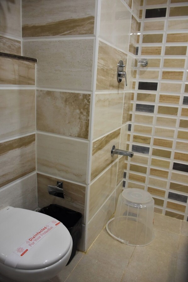 Un bagno con il water, un cestino e una zona doccia con pareti e pavimento piastrellati.