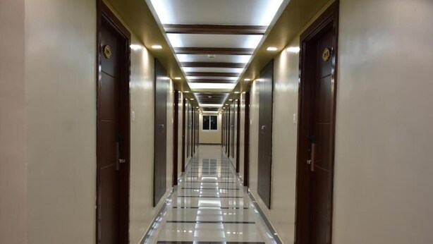 A long, narrow hallway with doors on both sides, a tiled floor, and a ceiling with recessed lighting. - Sri Ram Grand Inn (Palayankottai)