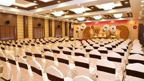 A conference room with rows of chairs, a stage with a decorative backdrop, and a ceiling with recessed lighting. - Sri Ram Grand Inn (Palayankottai)