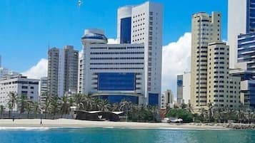 Paisatge urbà costaner amb edificis moderns alts, una platja i aigua blava i cristal·lina.