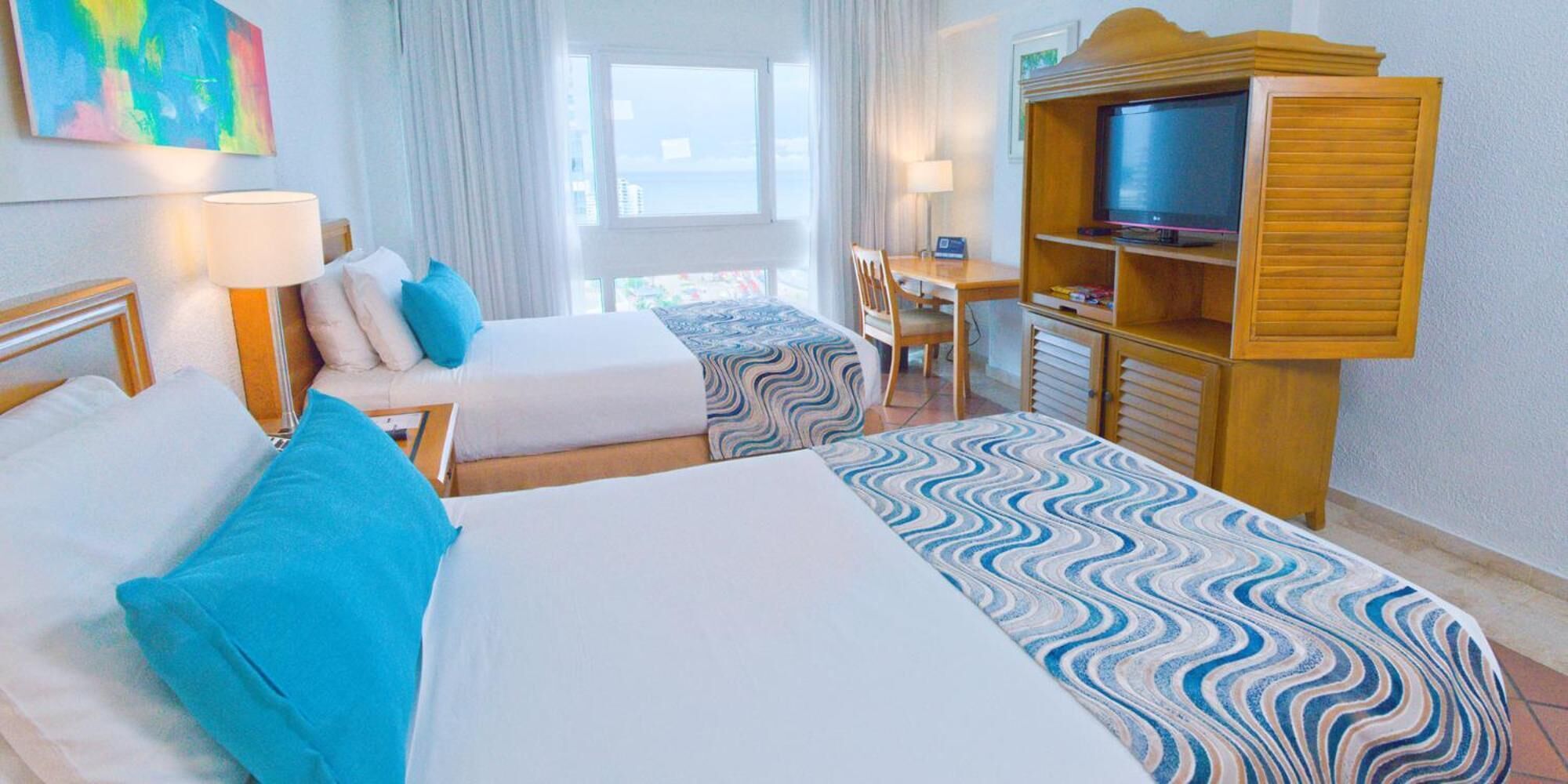 A hotel room with two beds, a TV, a desk, and a chair.