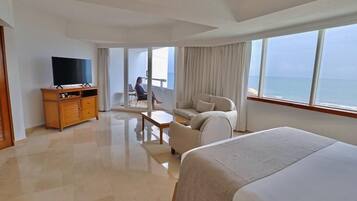 Habitació d'hotel amb llit, televisió, sofà, taula petita i balcó amb vistes al mar.