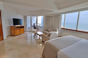 Habitación de hotel con cama, televisor, sofá, una mesita y balcón con vista al mar.