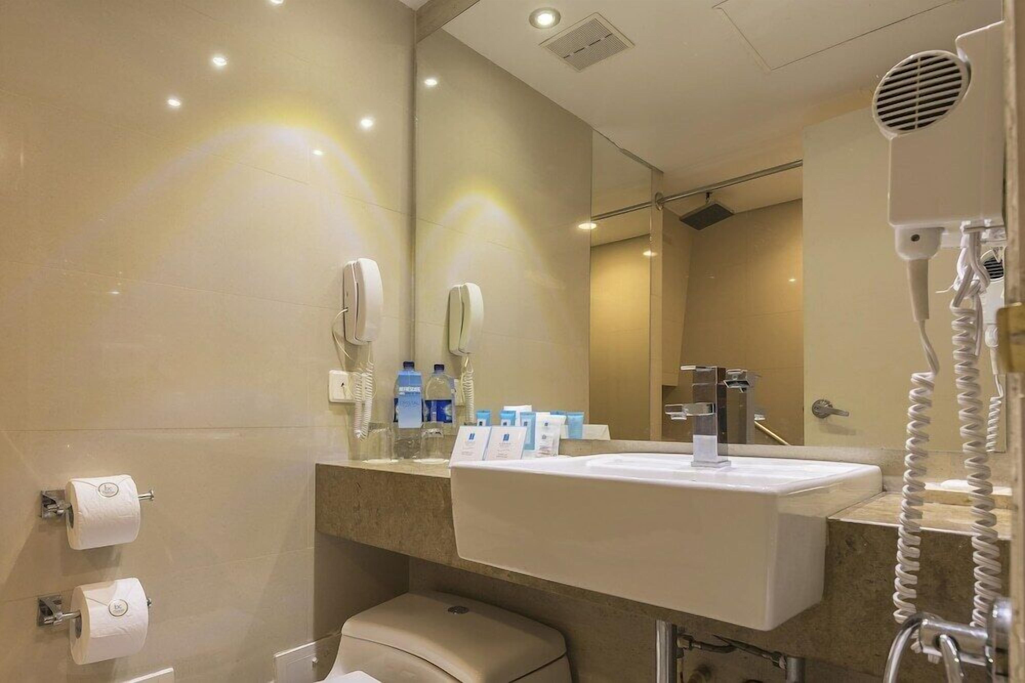 A modern bathroom with a sink, mirror, hairdryer, and toiletries.