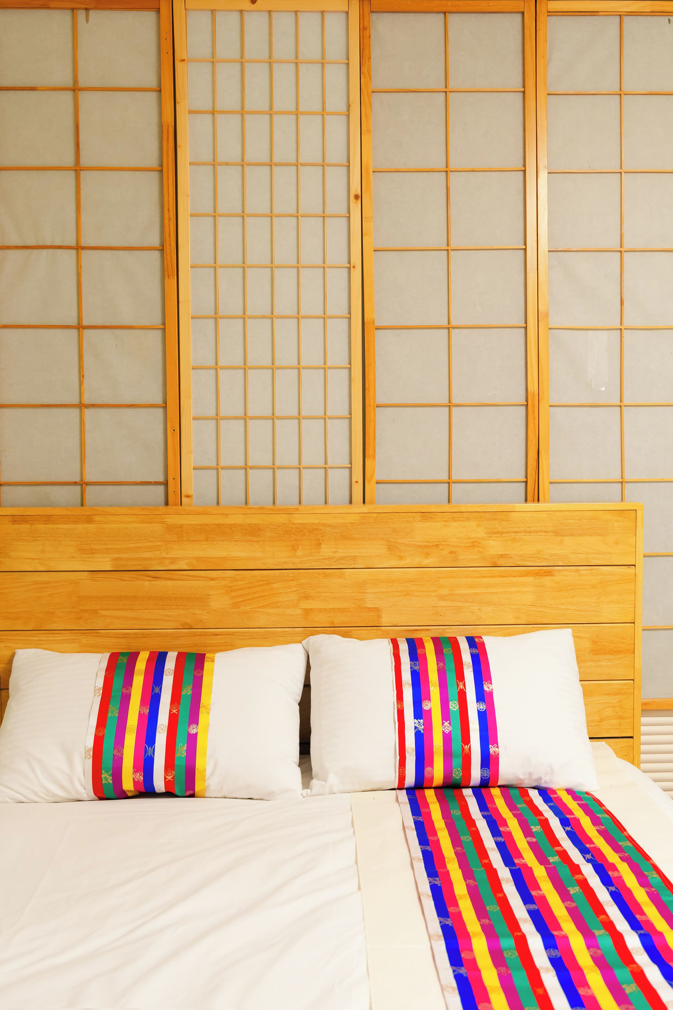 Una cama con cabecera de madera, ropa de cama blanca y almohadas coloridas a rayas.