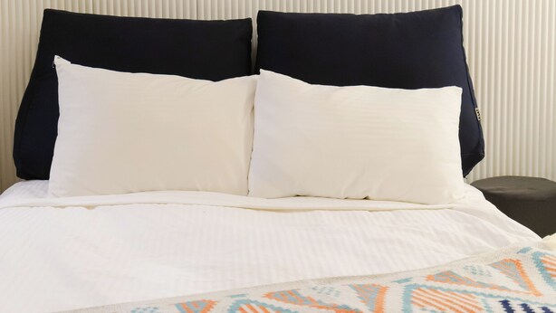 A bed with two pillows, a patterned blanket, and a white wall with vertical lines. - DREAM STAY (Seoul)