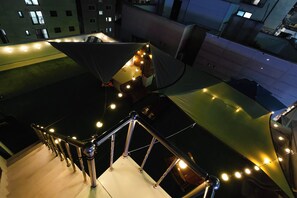 A rooftop terrace with a metal railing, string lights, and a view of surrounding buildings. - DREAM STAY (Seoul)