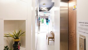 A hallway with a modern elevator, a potted plant, and a wooden bench. - DREAM STAY (Seoul)