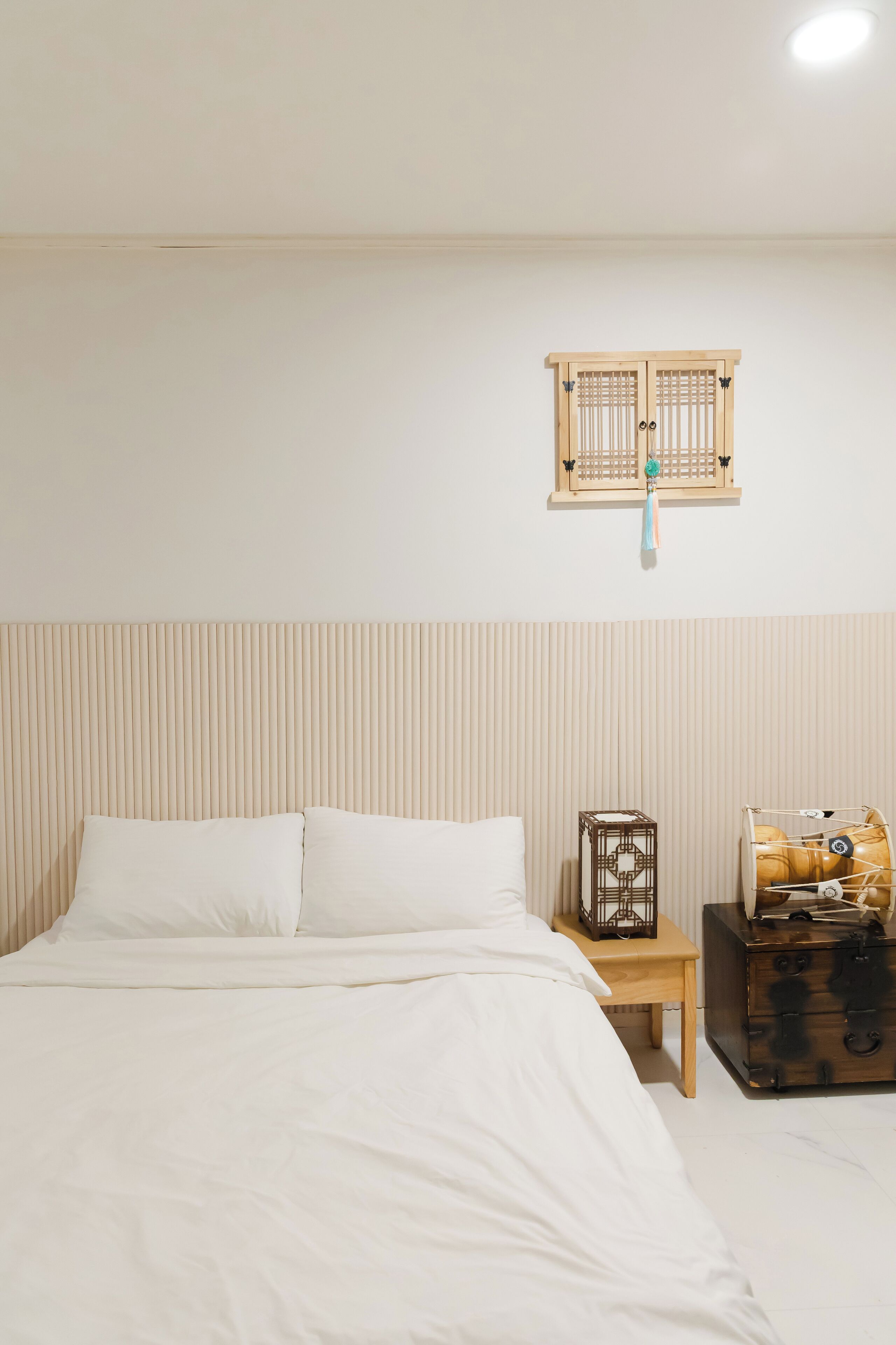 Un dormitorio con una cama, una mesita de noche de madera, una estantería decorativa y una maleta.
