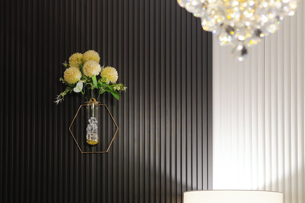 A wall with a geometric-patterned design, a wall-mounted lamp, and a decorative vase with flowers.