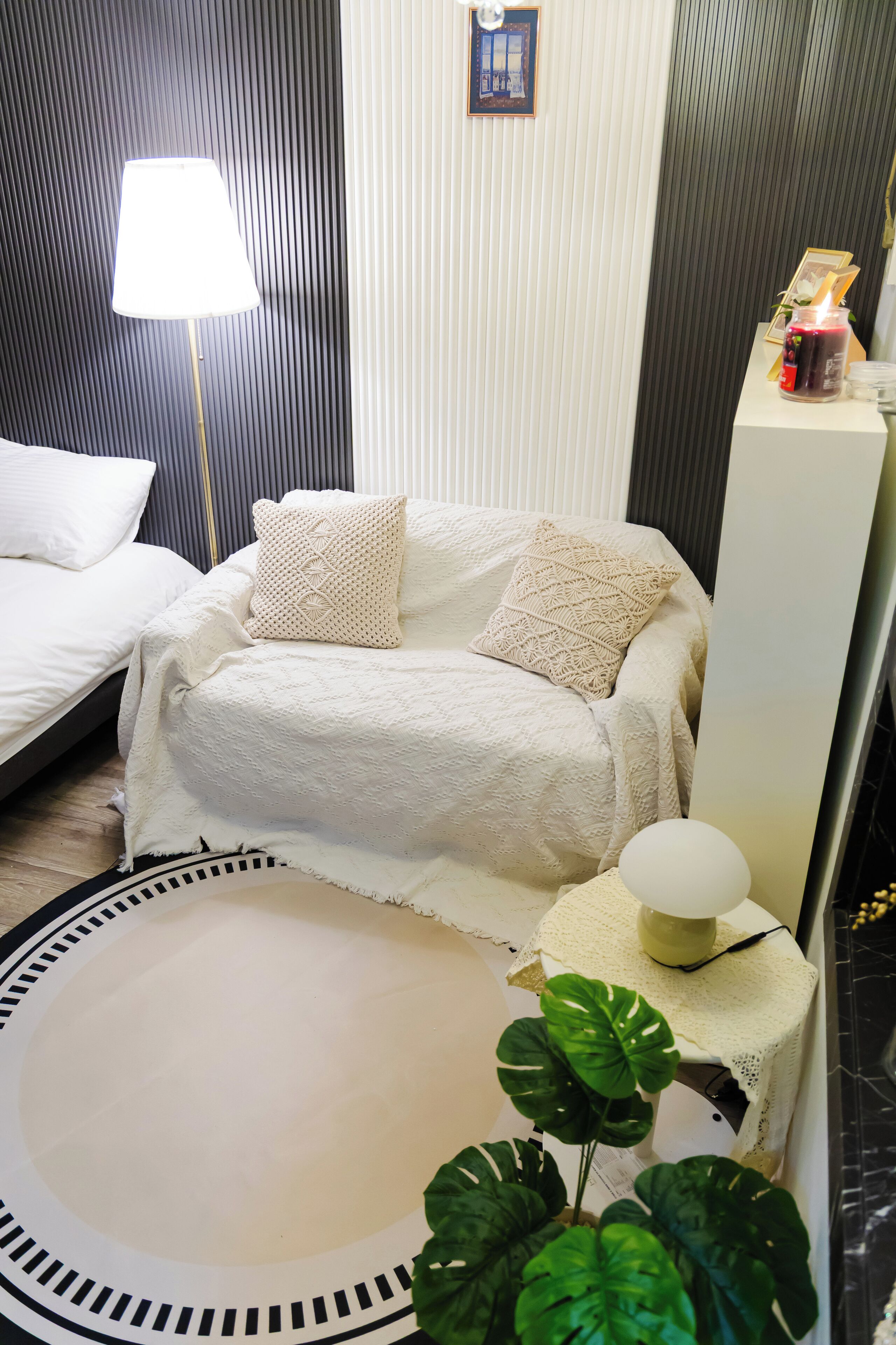 A bedroom with a bed, a sofa, a lamp, a small table, and a plant.