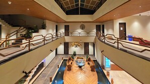 Un hall d’hôtel à plusieurs niveaux, doté d’un élément décoratif central en eau, de rampes en bois et d’un plafond haut.