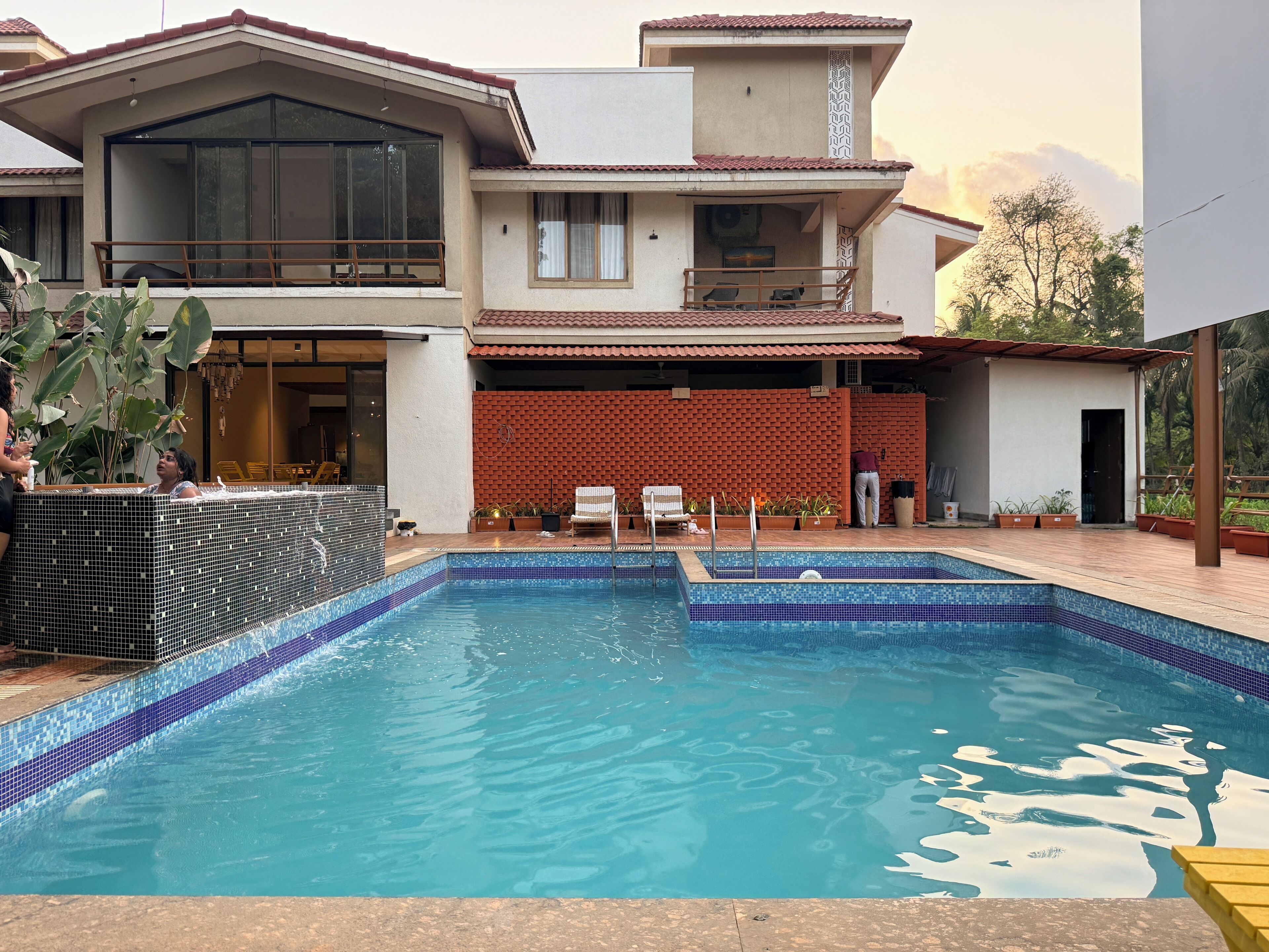 A two-story house with a swimming pool, a balcony, and a brick wall.