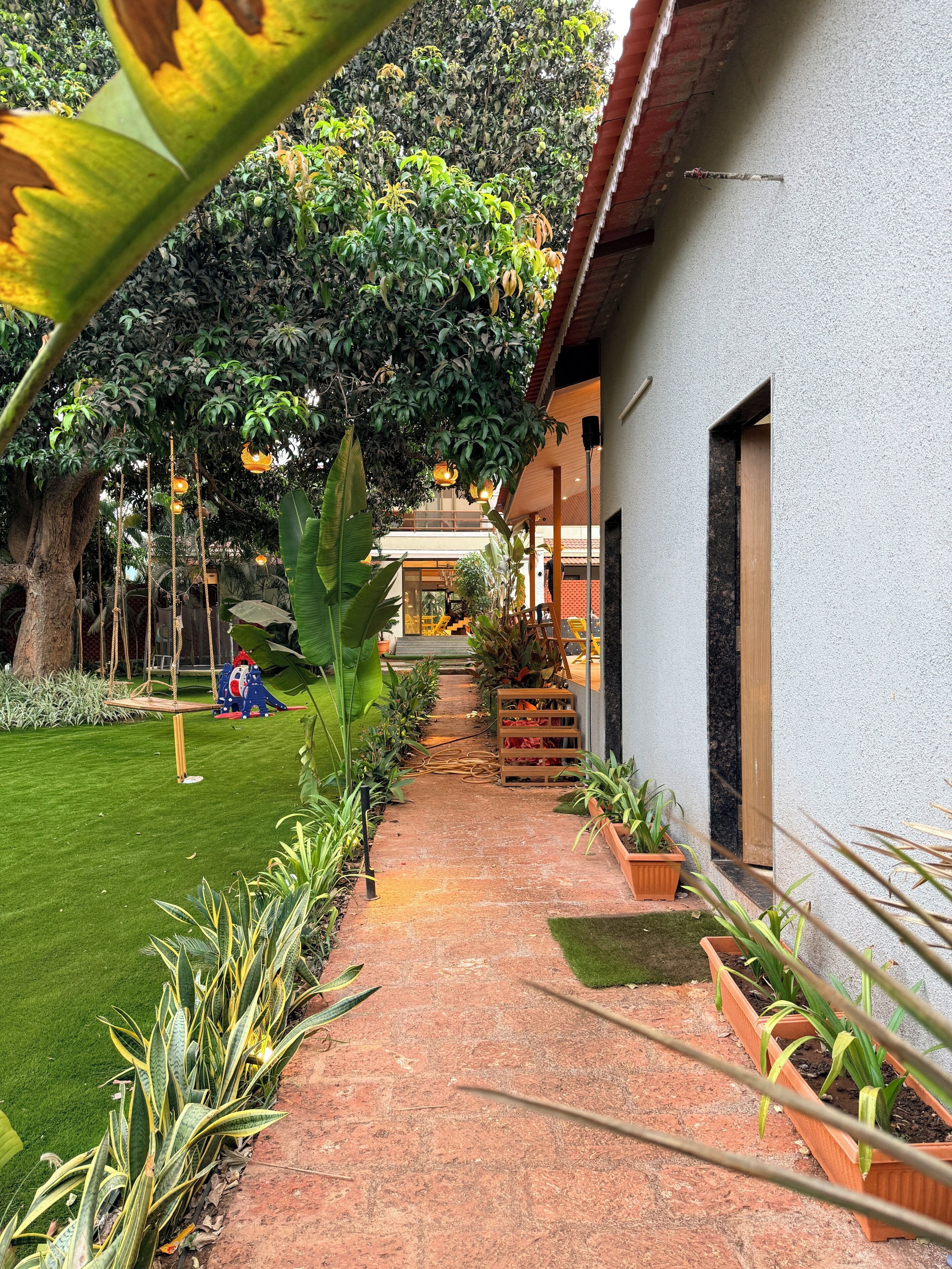 A pathway leading to a building with a garden area, potted plants, and a swing set.