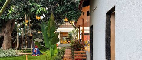 A pathway leading to a building with a garden area, potted plants, and a swing set.