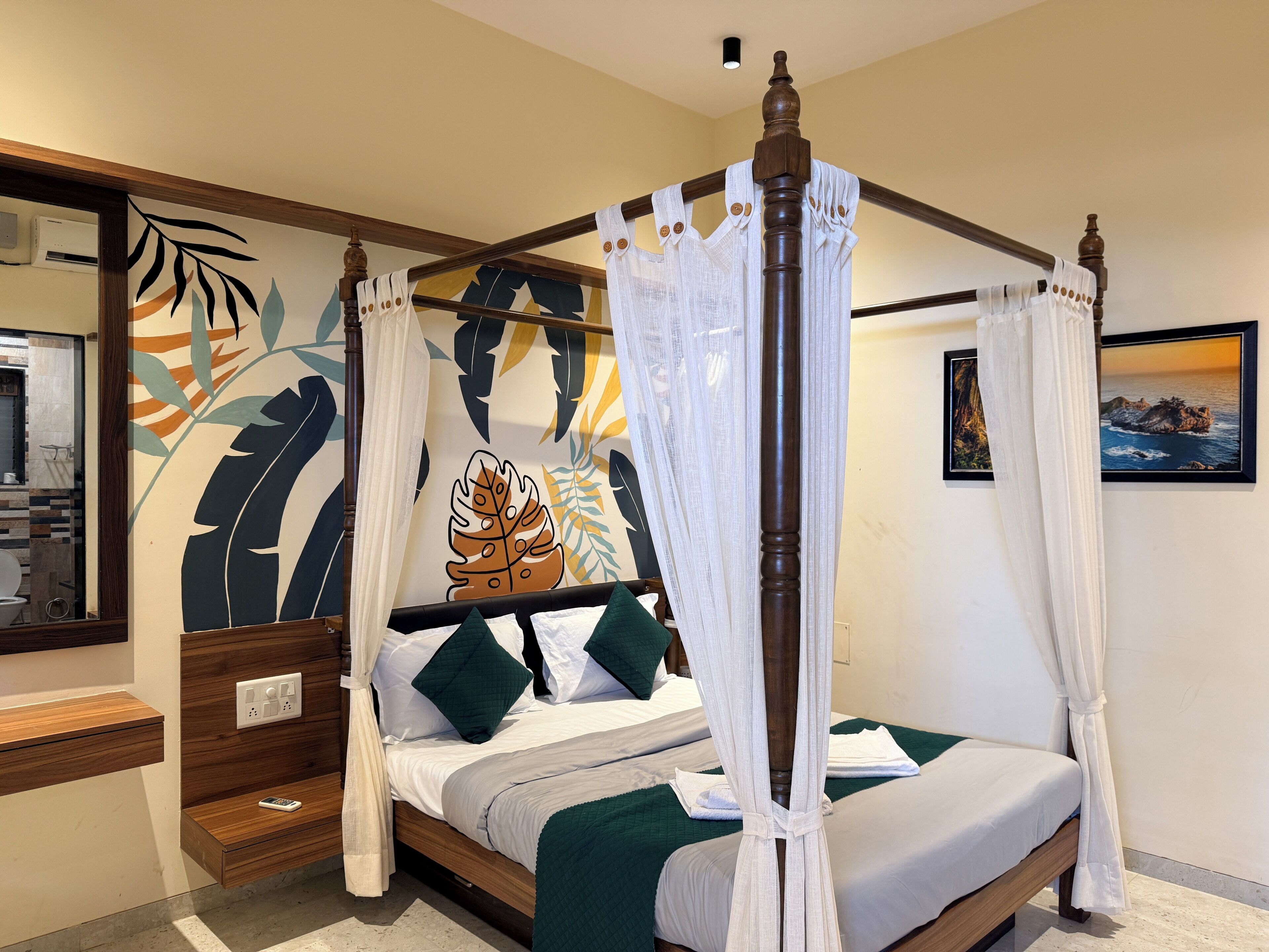 A four-poster bed with a canopy, a mirror, a wall with a leaf pattern, and a framed picture.