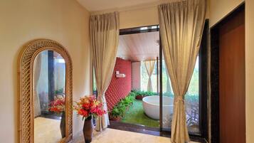 Un pasillo con un espejo grande, un jarrón con flores y vistas a un jardín con jacuzzi.
